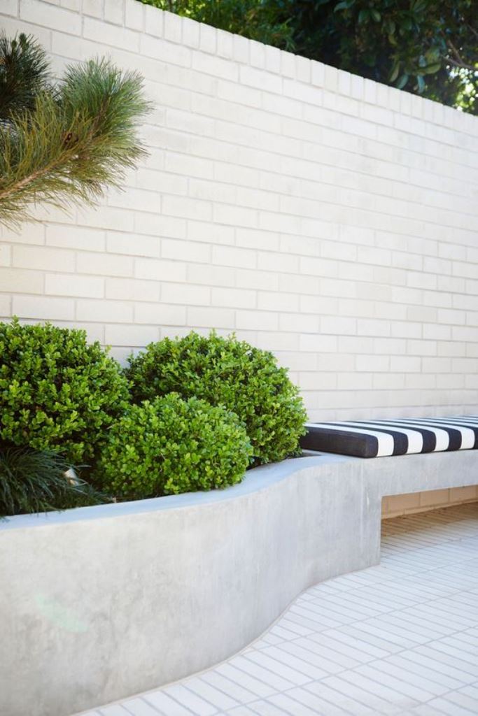 The concrete curved raised garden bed includes a bench, and this combo looks very bold.
