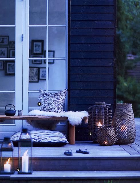 A Nordic summer terrace in black and white, with a bench, faux fur, pillows, wicker and glass candle holders.