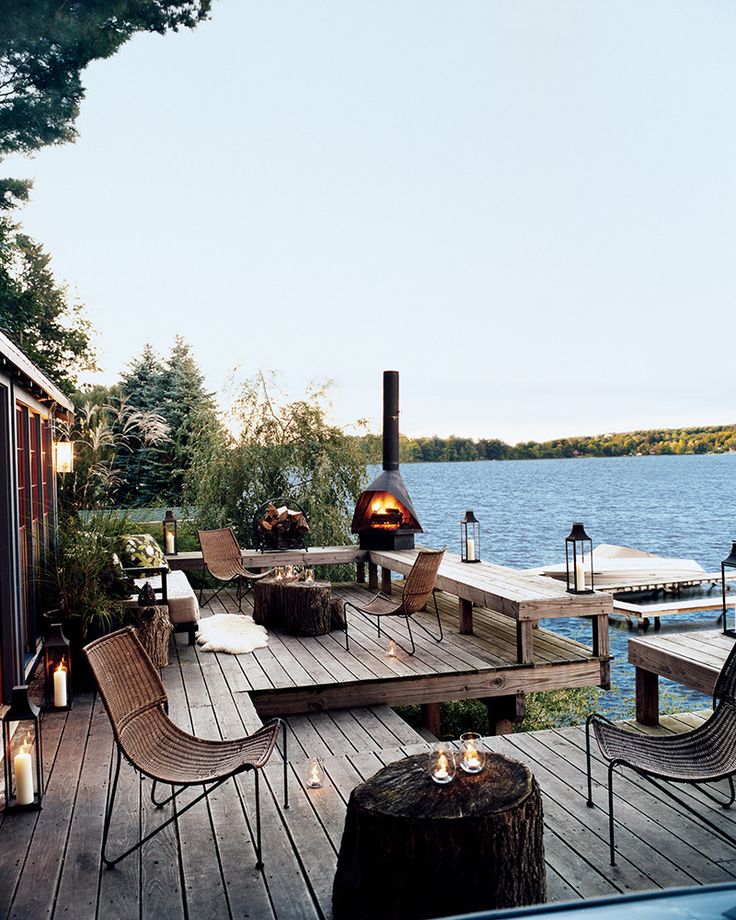 A riverside deck with wicker chairs, a fireplace, candle lanterns, stump tables and a cool riverside view.