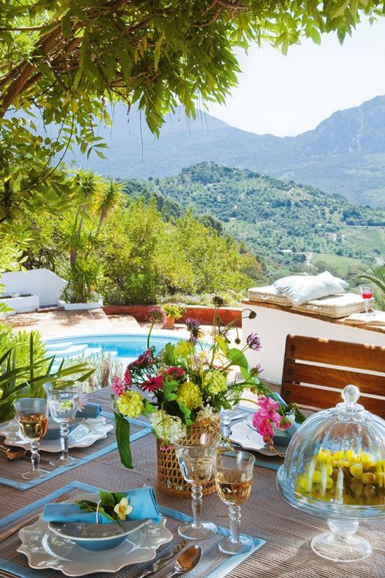 A bright summer terrace by the pool, with cushions and pillows and a bright dining zone with bold blooms and placemats with blue edges.