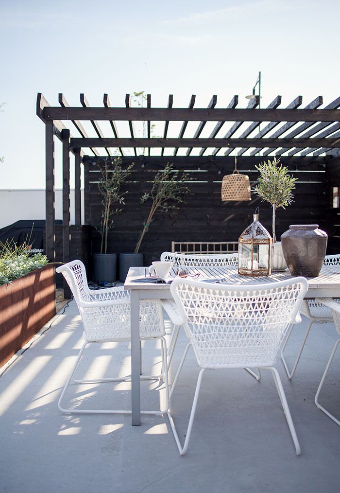 A monochromatic summer terrace with potted greenery and trees, white furniture of metal and wood, candle lanterns.