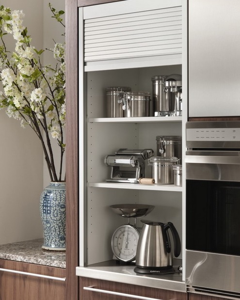 A narrow cabinet with shelves holding cookware, pots, some appliances can be closed with a shutter.