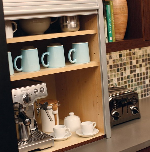 A storage cabinet with a coffee machine, mugs and cups and sugar is a mini coffee station with a shutter sliding down.