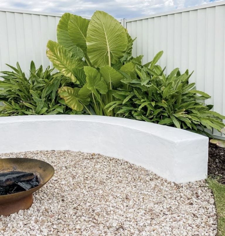 The corner shows off a lush green arrangement with a white slab bench and a fire bowl.