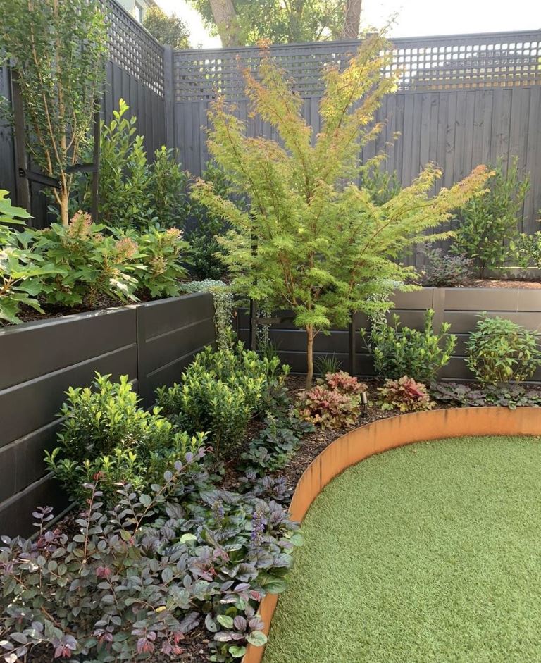 The fence is styled with a matching corner planter with greenery and a curved garden bed with corten steel edges.
