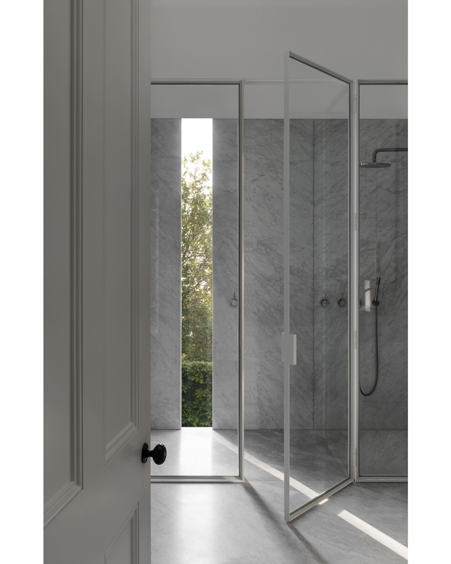 A narrow floor-to-ceiling window quietly transforms this minimalist marble shower, flooding it with gentle greenery views while maintaining total privacy.

(@alirossdesign).