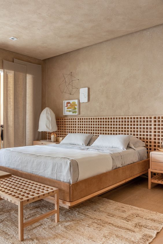The earthy bedroom is done with limewashed walls and ceiling, an upholstered bed with an added lattice headboard and a matching bench.