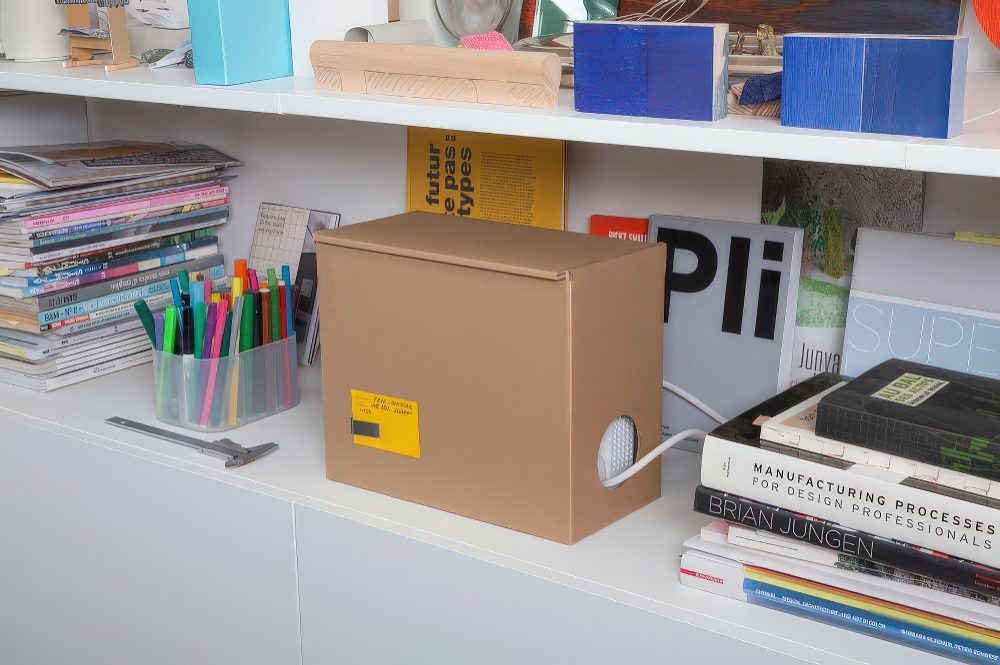 That cardboard box? Not a storage bin—it’s a disguise! Cutouts for wires keep everything neat, while the rest of your shelf stays stylish.

(@oscar_lhermitte).