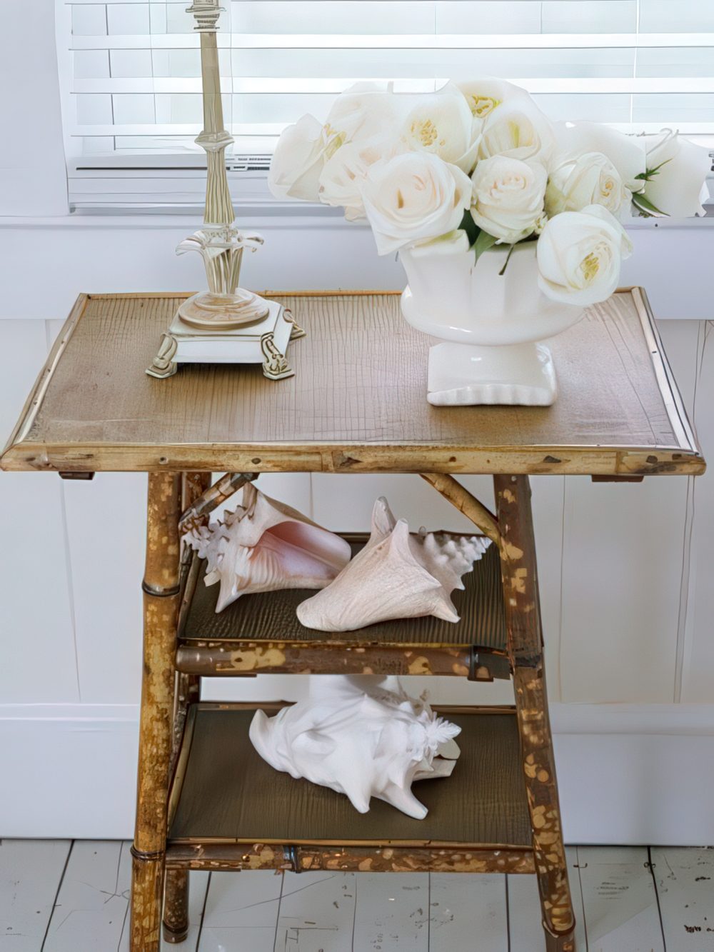 A rustic console table covered with burlap and with large shells and white blooms for beachy decor.
