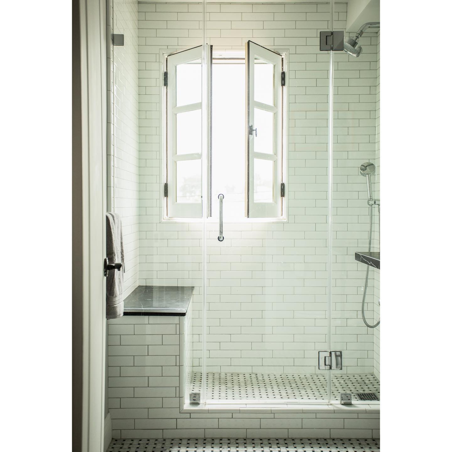 This bright walk-in shower features a charming double window that lets in plenty of daylight. The black bench adds a subtle modern edge to the all-white subway tile walls and classic glass door.
(@backup_design).