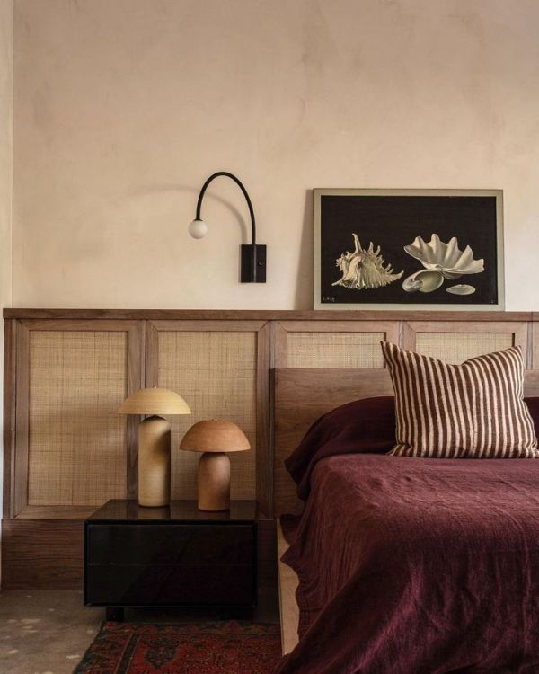 The moody space with a stained bed and framed linen panels as a headboard, with decor and lamps over it.