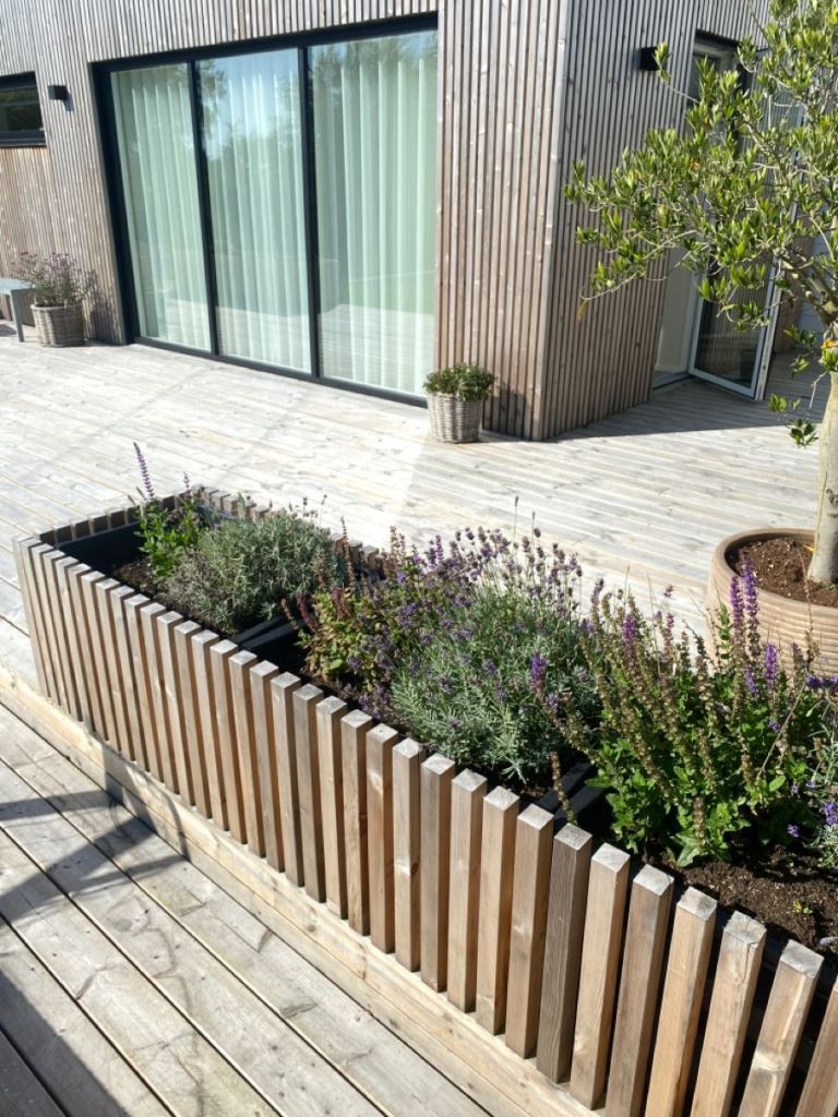 The narrow long modern planter is clad with slats and features simple grasses and blooms for a contemporary feel.