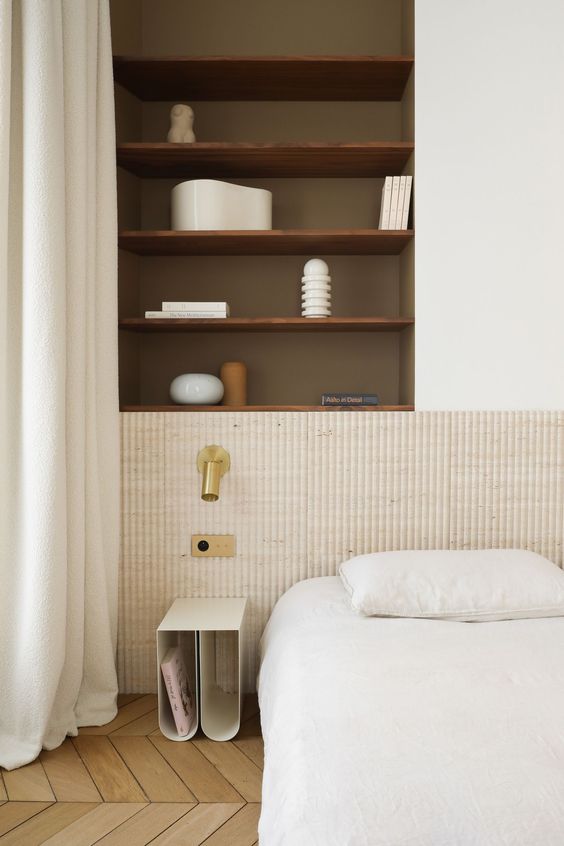The serene space is done with a neutral ribbed headboard, a bed and a small nightstand, built-in shelves.