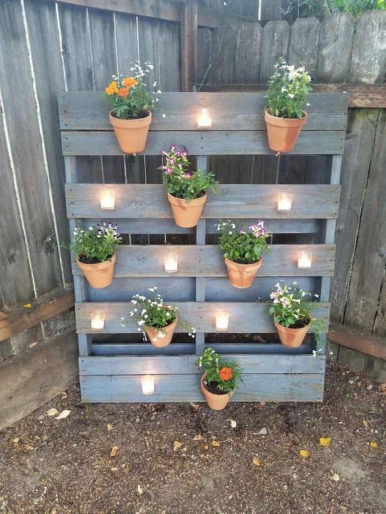 The reclaimed wood pallet is used to make a vertical garden with candles and pots attached to it.