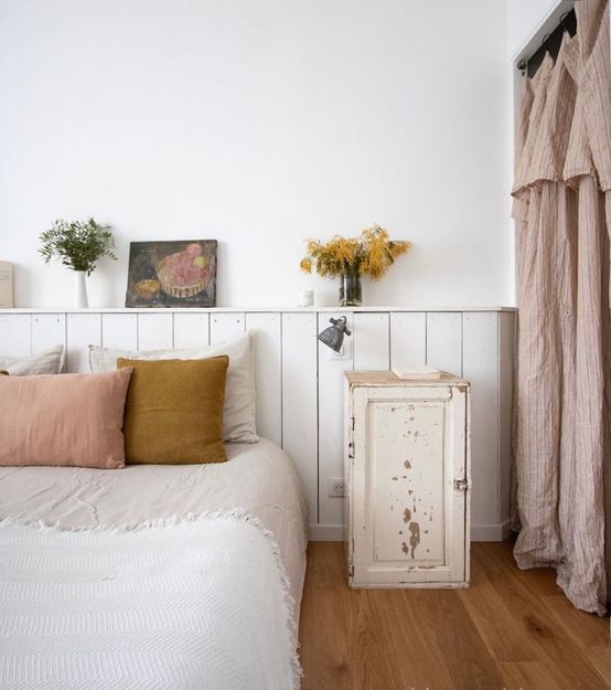 The neutral sleeping space is done with a bed and a white planked headboard with a shelf, with decor, a shabby chic nightstand.
