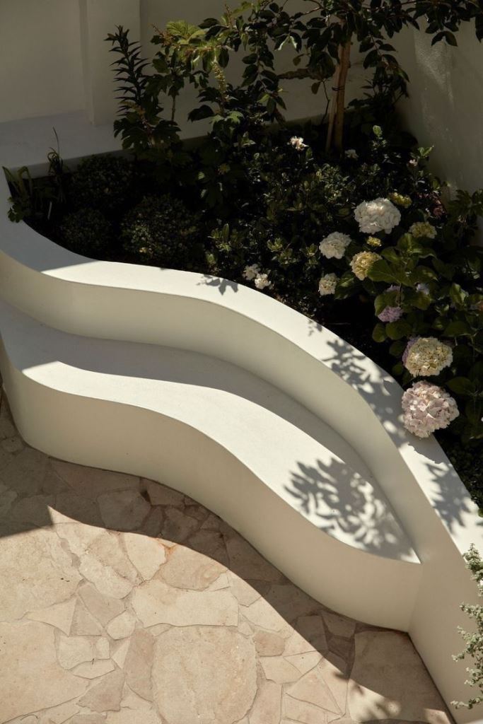 The minimalist corner raised garden bed includes a bench and lush hydrangeas.