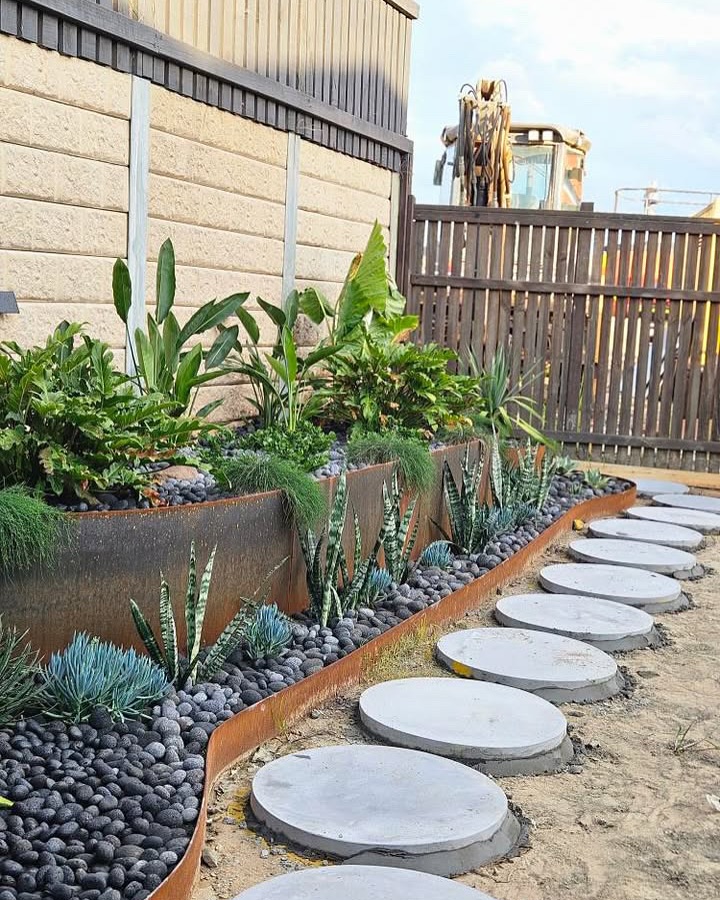 A metal garden border combined with dark stones and structured plant choices like snake plants and blue fescue creates a polished, contemporary look. This is a smart way to separate planting areas, add dimension, and keep mulch or gravel in place while defining pathways.

(@straightcurvegardenedge).
