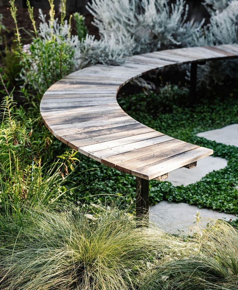 This reclaimed wooden bench is curved to elevate the style of the space, and lush greenery and grasses make the space feel modern.