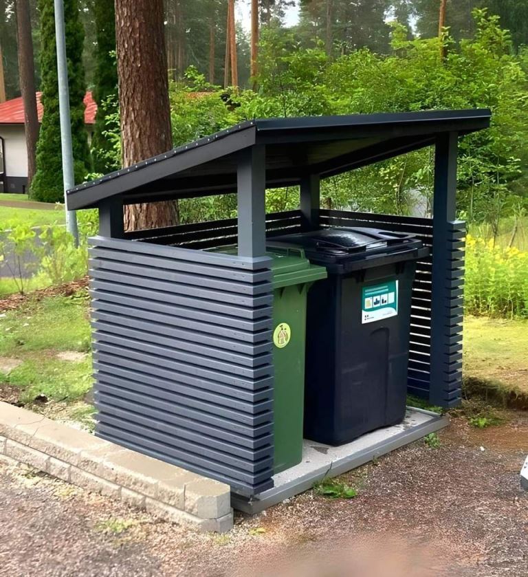 These trash cans are hidden with black slatted screens and the roof protects them from rain.