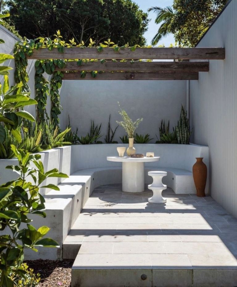 The minimalist nook shows off a raised garden bed with succulents, a built-in bench and tables. Green vines refresh the space.