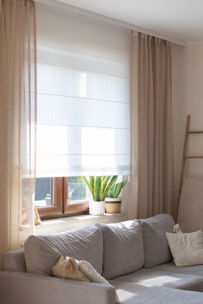 The white Roman shades and tan curtains make up nice layered treatments that block out all the unwanted things.