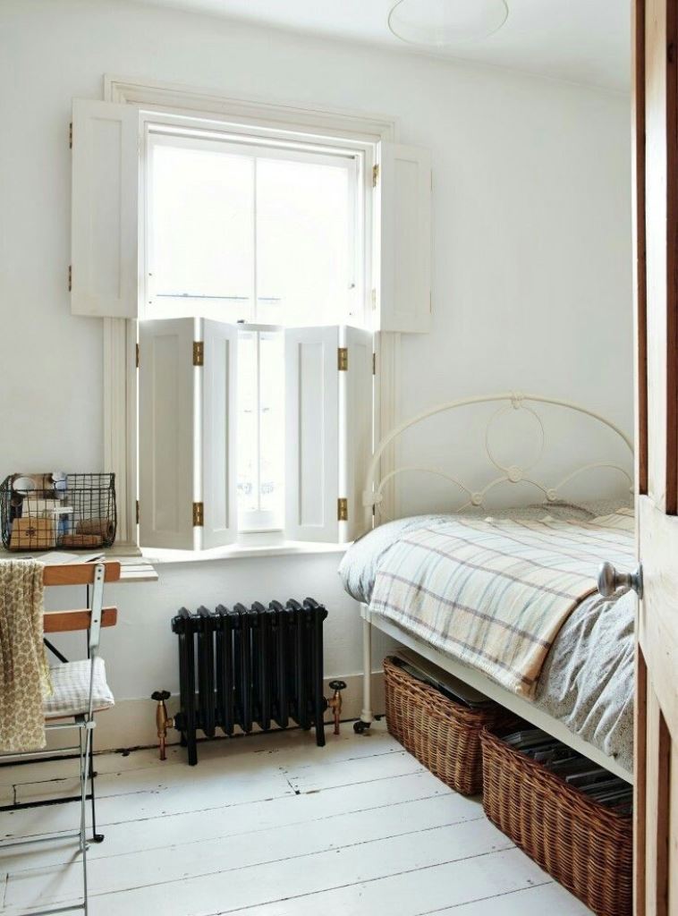 The bedroom is styled with a vintage feel, and creamy shutters on the window block the unwanted view.