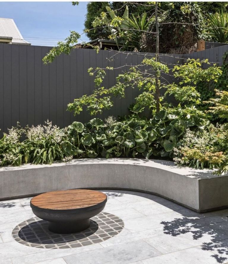 This contemporary garden corner is done with lush greenery, a curved slab bench and a coffee table.
