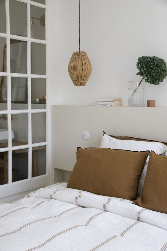 The neutral bedroom shows off a bed with an added tan storage headboard, with decor on top and a pendant lamp.
