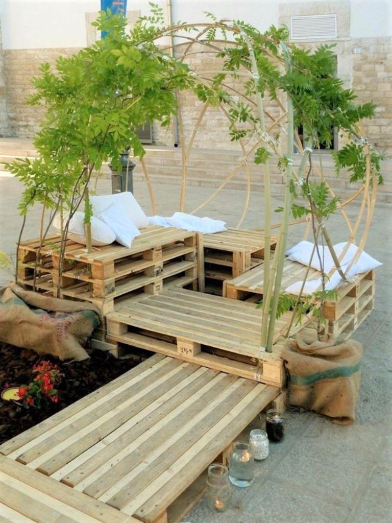 Stacked pallets form a whole combo of seats and daybeds, and the top of it is covered with vines.