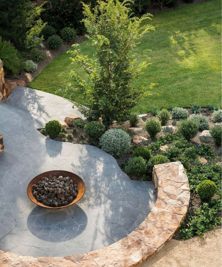 I adore this textural and sculptural lanscape with lots of greenery and a tree, a stone patio and a matching curved bench.