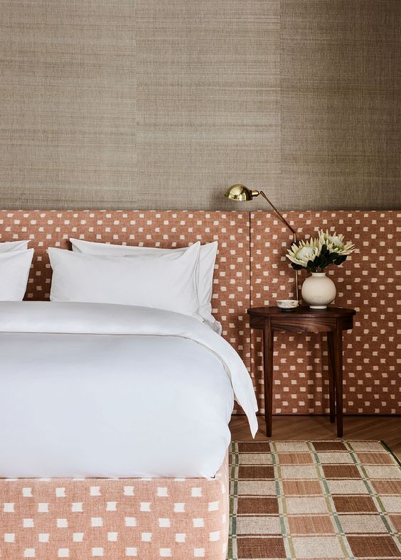 The bedroom is filled with texture, with grasscloth wallpaper, an upholstered bed with a matching extra wide feminine headboard and a printed rug.