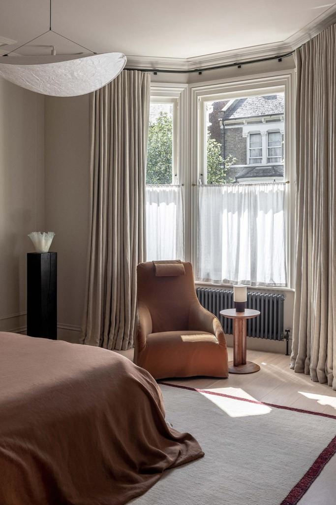 The bow window features white cafe curtains and neutral drapes to keep the bedroom private and block the views.