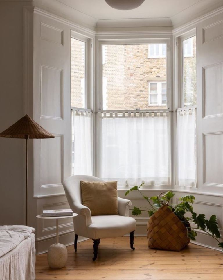 The bow window is treated both with cafe curtains and white shutters to match the vintage style of the bedroom.