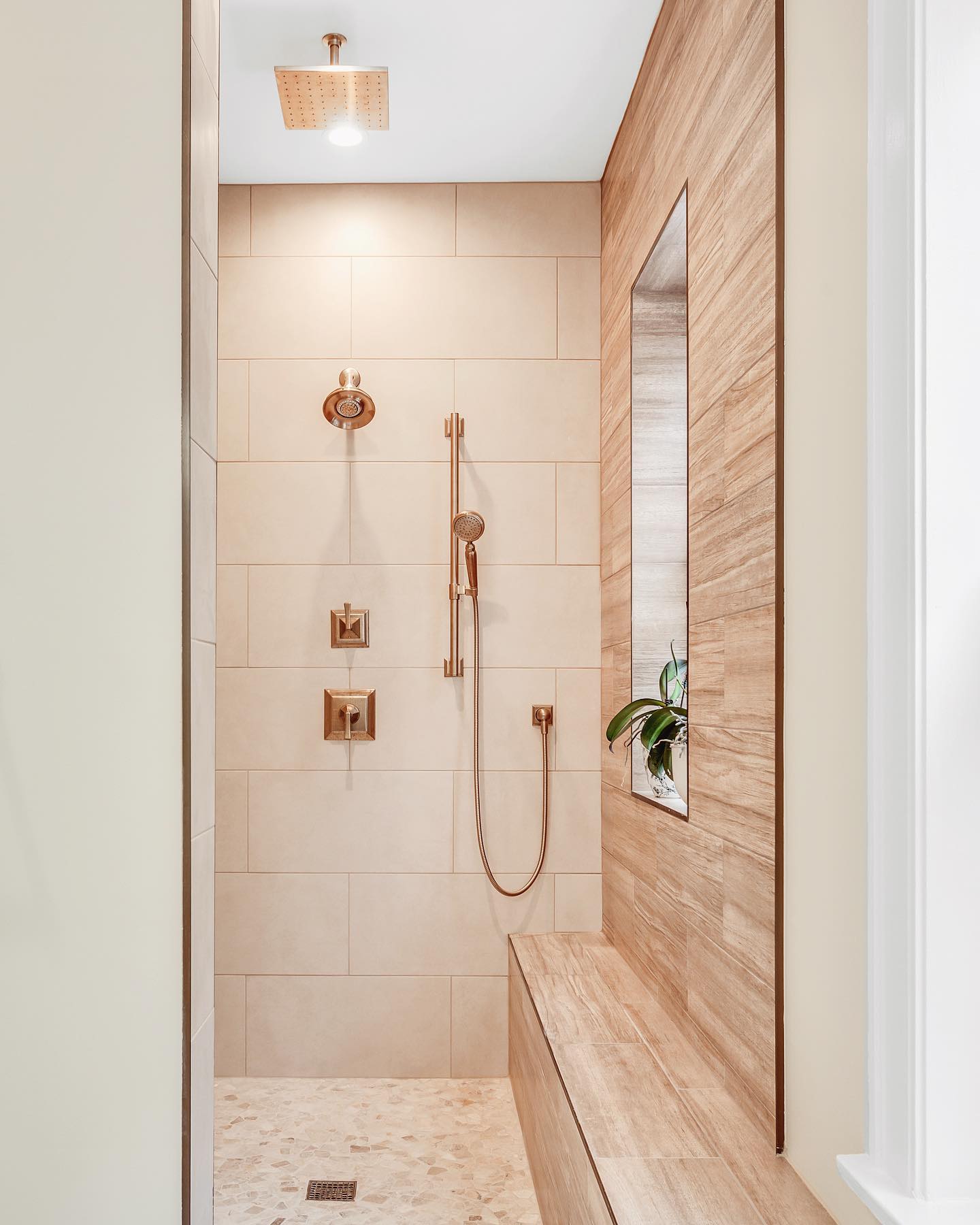 Warm wood tones and a bench – A large built-in bench and wood-look tile give this shower warmth, while a narrow niche and a hidden window bring in light without compromising style.

(@magdainteriors_).