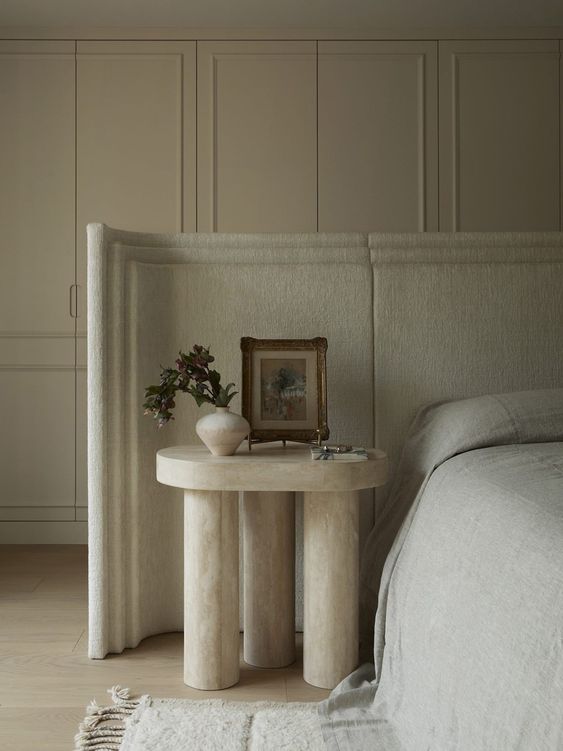 The neutral and sophisticated bedroom is done with panels on the walls, an upholstered wingback headboard and a stone nightstand.